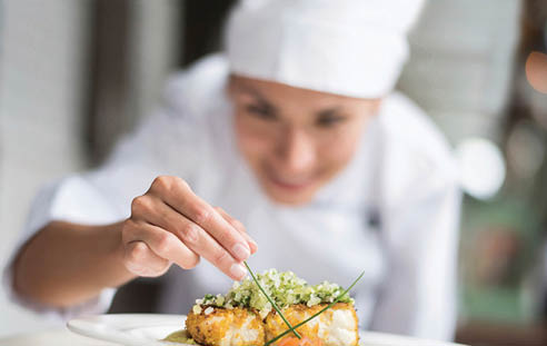 Cook decorating a plate and putting the ultimate touches - focus on foreground 