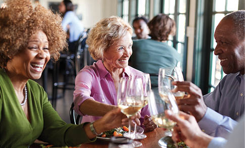 Three people are sitting at a table, enjoying a meal and drinking wine. They are smiling and having a good time. AI generated content