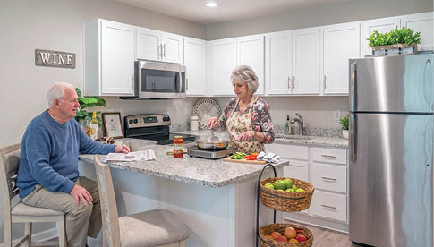 A kitchen with a refrigerator, microwave, and sink. The refrigerator is silver and has a potted plant on top. There are two chairs and a dining table in the kitchen. AI generated content