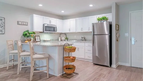 A kitchen with a refrigerator, microwave, and sink. The refrigerator is silver and has a potted plant on top. There are two chairs and a dining table in the kitchen. AI generated content