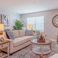 A living room with a couch, chair, and coffee table. A clock on the wall, a potted plant, and a vase with flowers on the table. AI generated content