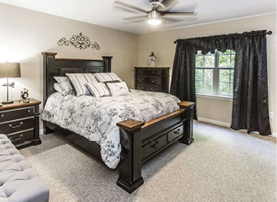 A bedroom with a bed, dresser, and nightstand. The bed has a black headboard and a white and black comforter. The room also has a window with black curtains. AI generated content